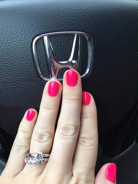 A hand with hot pink nails resting on a steering wheel